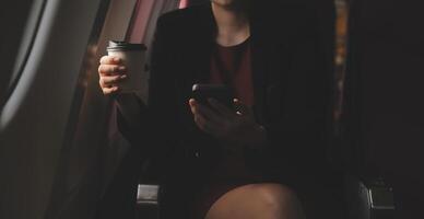 Blonde female tourist checking incoming notification on smartphone sitting on seat of airplane with netbook.Young businesswoman share media from telephone on laptop computer during plane flight photo