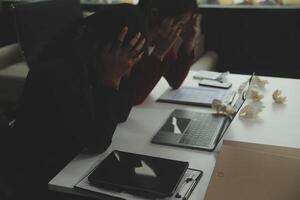 Stressed annoyed office employee manager having headache migraine at business meeting with his colleagues about business problem they have to solve. Stress at work or migraine concept. photo