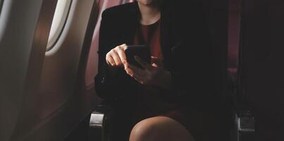 Blonde female tourist checking incoming notification on smartphone sitting on seat of airplane with netbook.Young businesswoman share media from telephone on laptop computer during plane flight photo