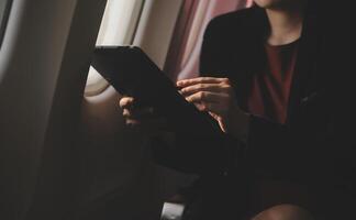 Blonde female tourist checking incoming notification on smartphone sitting on seat of airplane with netbook.Young businesswoman share media from telephone on laptop computer during plane flight photo
