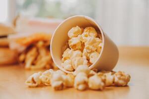 A bucket of popcorn, top-view, warm colors, light brown wooden background, flat lay, daylight macro close-up photo