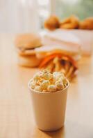A bucket of popcorn, top-view, warm colors, light brown wooden background, flat lay, daylight macro close-up photo