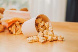 A bucket of popcorn, top-view, warm colors, light brown wooden background, flat lay, daylight macro close-up photo