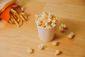 A bucket of popcorn, top-view, warm colors, light brown wooden background, flat lay, daylight macro close-up photo