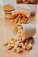 A bucket of popcorn, top-view, warm colors, light brown wooden background, flat lay, daylight macro close-up photo