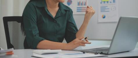 Asian Businesswoman Using laptop computer and working at office with calculator document on desk, doing planning analyzing the financial report, business plan investment, finance analysis concept. photo