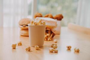 A bucket of popcorn, top-view, warm colors, light brown wooden background, flat lay, daylight macro close-up photo