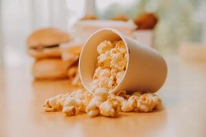 A bucket of popcorn, top-view, warm colors, light brown wooden background, flat lay, daylight macro close-up photo
