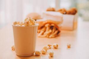 A bucket of popcorn, top-view, warm colors, light brown wooden background, flat lay, daylight macro close-up photo