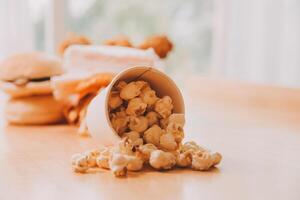A bucket of popcorn, top-view, warm colors, light brown wooden background, flat lay, daylight macro close-up photo