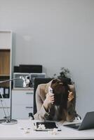 Asian women sitting in an office With stress and eye strain Tired, portrait of sad unhappy tired frustrated disappointed lady suffering from migraine sitting at the table, Sick worker concept photo