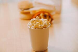 A bucket of popcorn, top-view, warm colors, light brown wooden background, flat lay, daylight macro close-up photo