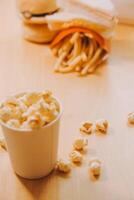 A bucket of popcorn, top-view, warm colors, light brown wooden background, flat lay, daylight macro close-up photo