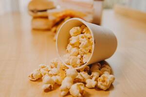 A bucket of popcorn, top-view, warm colors, light brown wooden background, flat lay, daylight macro close-up photo