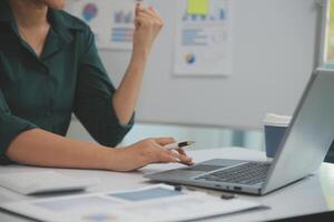 Asian Businesswoman Using laptop computer and working at office with calculator document on desk, doing planning analyzing the financial report, business plan investment, finance analysis concept. photo