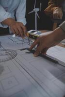 Team of multiethnic architects working on construction plans in meeting room. Engineers discussing on project in office. Mature businessman and woman standing around table working on blueprint. photo