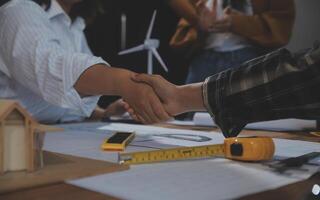 Construction team shake hands greeting start new project plan behind yellow helmet on desk in office center to consults about their building project. in sun light photo