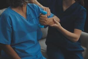 Old woman training with physiotherapist using dumbbells at home. Therapist assisting senior woman with exercises in nursing home. Elderly patient using dumbbells with outstretched arms. photo