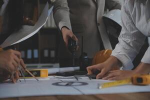 Team of multiethnic architects working on construction plans in meeting room. Engineers discussing on project in office. Mature businessman and woman standing around table working on blueprint. photo