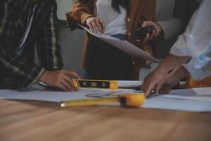Team of multiethnic architects working on construction plans in meeting room. Engineers discussing on project in office. Mature businessman and woman standing around table working on blueprint. photo