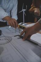 Team of multiethnic architects working on construction plans in meeting room. Engineers discussing on project in office. Mature businessman and woman standing around table working on blueprint. photo