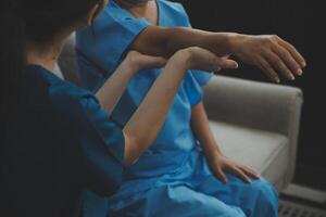 Old woman training with physiotherapist using dumbbells at home. Therapist assisting senior woman with exercises in nursing home. Elderly patient using dumbbells with outstretched arms. photo