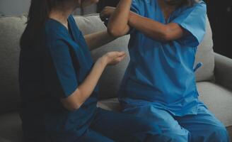 Old woman training with physiotherapist using dumbbells at home. Therapist assisting senior woman with exercises in nursing home. Elderly patient using dumbbells with outstretched arms. photo