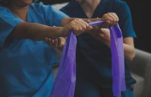 Personal trainer assisting senior woman with resistance band. Rehabilitation physiotherapy worker helping old patient at nursing home. Old woman with stretch band being coached by physiotherapist. photo