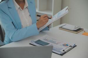 Charming Young asian businesswoman sitting on laptop computer in the office, making report calculating balance Internal Revenue Service checking document. photo