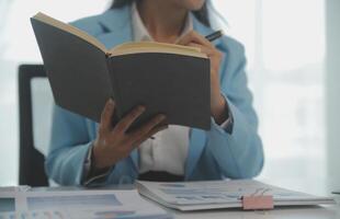 Charming Young asian businesswoman sitting on laptop computer in the office, making report calculating balance Internal Revenue Service checking document. photo