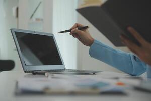 Charming Young asian businesswoman sitting on laptop computer in the office, making report calculating balance Internal Revenue Service checking document. photo