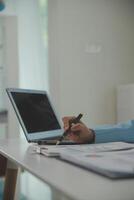 Charming Young asian businesswoman sitting on laptop computer in the office, making report calculating balance Internal Revenue Service checking document. photo