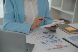 Charming Young asian businesswoman sitting on laptop computer in the office, making report calculating balance Internal Revenue Service checking document. photo