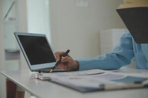 Charming Young asian businesswoman sitting on laptop computer in the office, making report calculating balance Internal Revenue Service checking document. photo