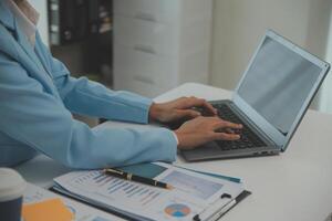 Charming Young asian businesswoman sitting on laptop computer in the office, making report calculating balance Internal Revenue Service checking document. photo