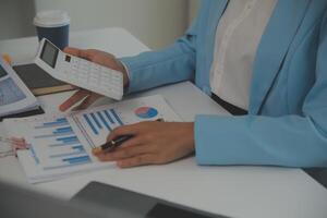 Charming Young asian businesswoman sitting on laptop computer in the office, making report calculating balance Internal Revenue Service checking document. photo