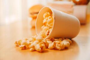 A bucket of popcorn, top-view, warm colors, light brown wooden background, flat lay, daylight macro close-up photo