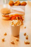 A bucket of popcorn, top-view, warm colors, light brown wooden background, flat lay, daylight macro close-up photo