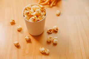 A bucket of popcorn, top-view, warm colors, light brown wooden background, flat lay, daylight macro close-up photo