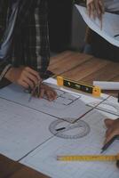 Team of multiethnic architects working on construction plans in meeting room. Engineers discussing on project in office. Mature businessman and woman standing around table working on blueprint. photo