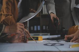 Team of multiethnic architects working on construction plans in meeting room. Engineers discussing on project in office. Mature businessman and woman standing around table working on blueprint. photo