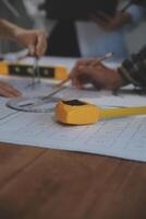 Team of multiethnic architects working on construction plans in meeting room. Engineers discussing on project in office. Mature businessman and woman standing around table working on blueprint. photo