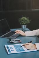 Asian Businesswoman Using laptop computer and working at office with calculator document on desk, doing planning analyzing the financial report, business plan investment, finance analysis concept. photo