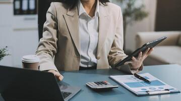 Asian Businesswoman Using laptop computer and working at office with calculator document on desk, doing planning analyzing the financial report, business plan investment, finance analysis concept. photo
