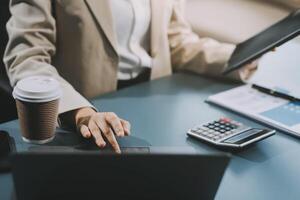 Asian Businesswoman Using laptop computer and working at office with calculator document on desk, doing planning analyzing the financial report, business plan investment, finance analysis concept. photo