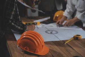 Team of multiethnic architects working on construction plans in meeting room. Engineers discussing on project in office. Mature businessman and woman standing around table working on blueprint. photo