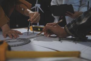 Team of multiethnic architects working on construction plans in meeting room. Engineers discussing on project in office. Mature businessman and woman standing around table working on blueprint. photo