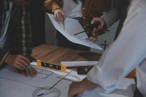 Team of multiethnic architects working on construction plans in meeting room. Engineers discussing on project in office. Mature businessman and woman standing around table working on blueprint. photo