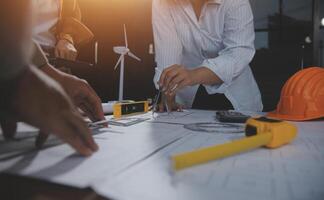 Team of multiethnic architects working on construction plans in meeting room. Engineers discussing on project in office. Mature businessman and woman standing around table working on blueprint. photo
