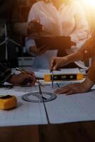 Team of multiethnic architects working on construction plans in meeting room. Engineers discussing on project in office. Mature businessman and woman standing around table working on blueprint. photo